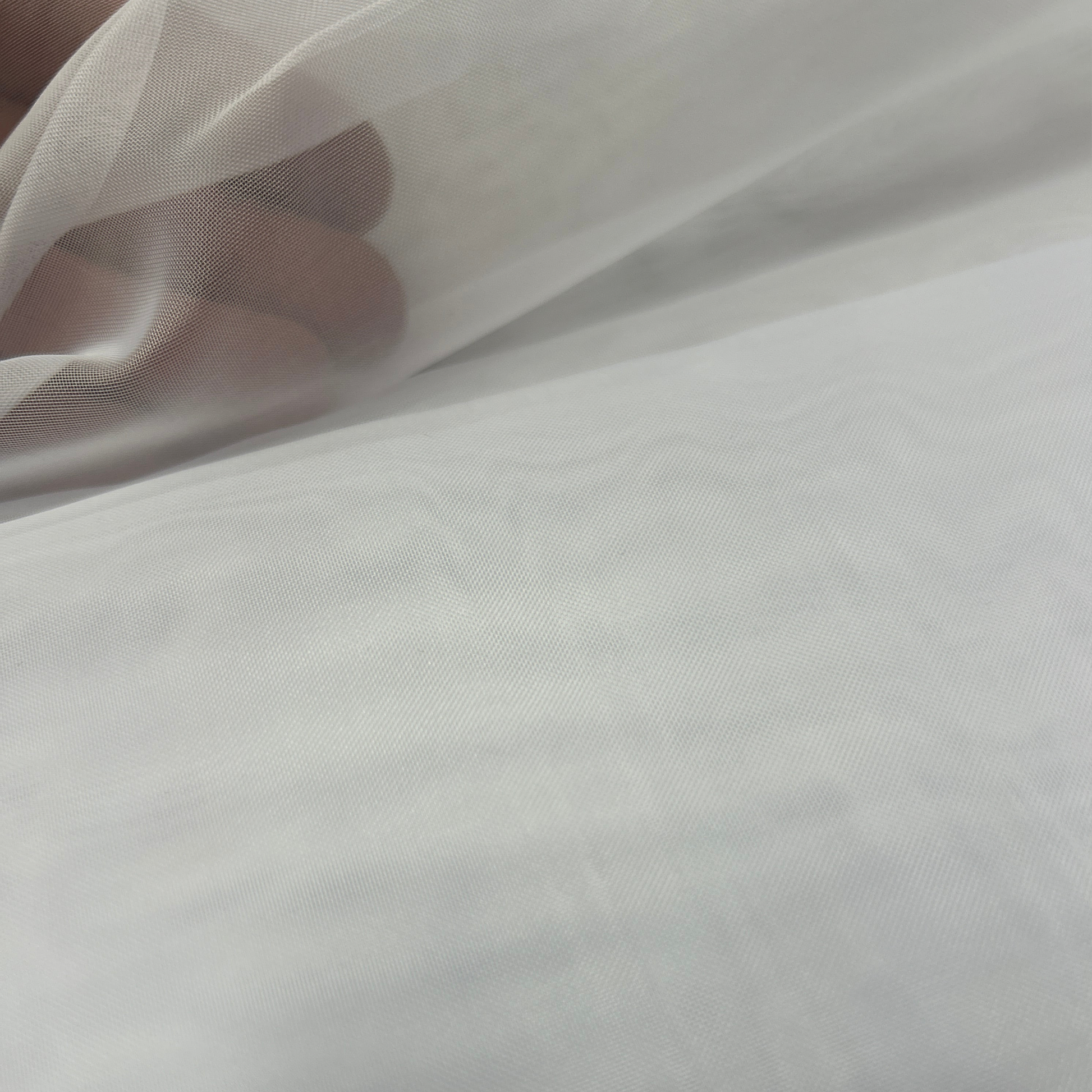 close up of white voile fabric showing sheer transparency with hand behind material